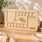 Close-up view of a blank custom oak light wood school years milestone photo frame standing on a studio table with decorative beads, showing the empty passport-sized photo slots and personalized laser engraving.