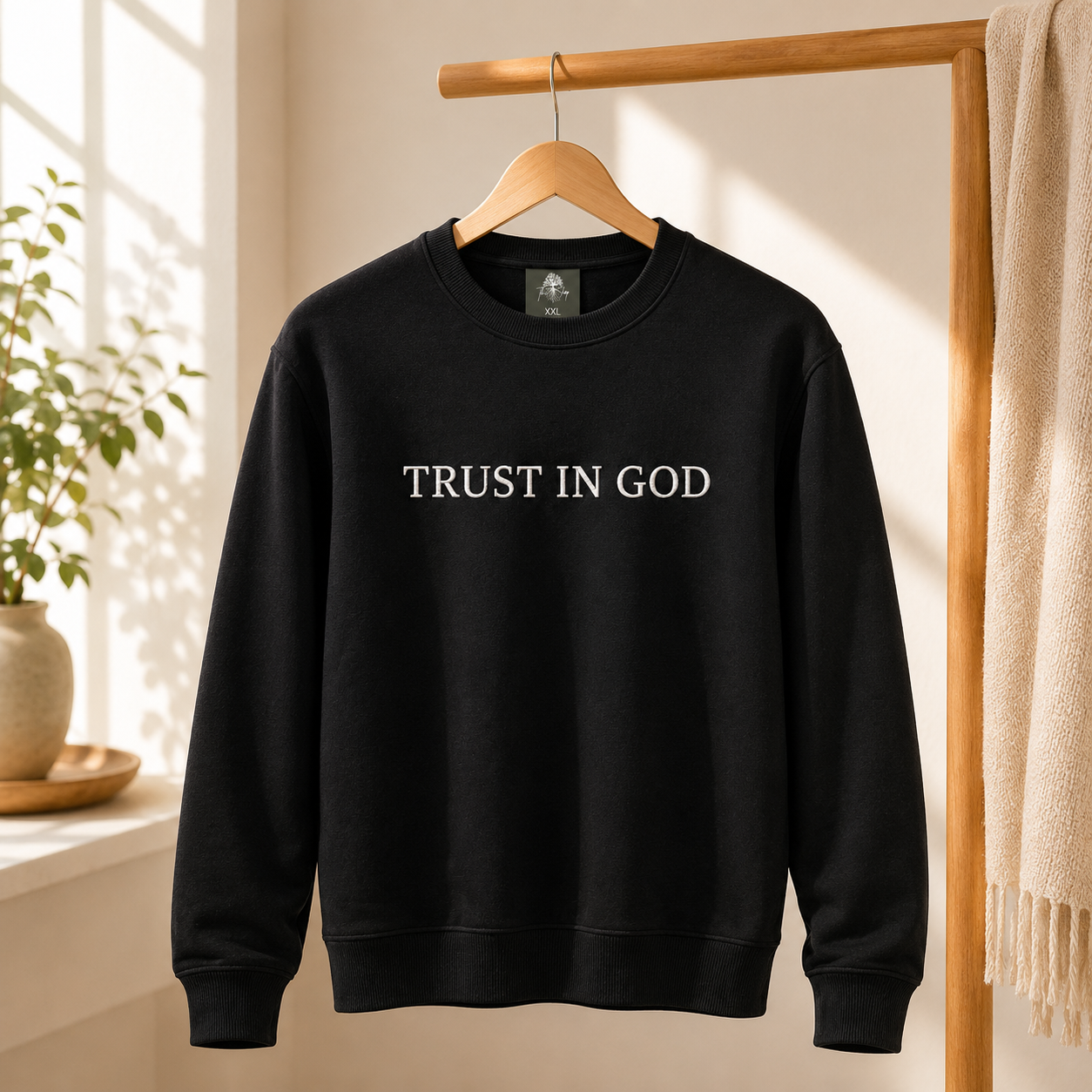 Close-up view of a classic black cotton blend crewneck sweater with minimalist white embroidered lettering displaying the phrase 'TRUST IN GOD'.
