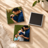 Three 2.5x2.5 inch personalized square glossy photo magnets showcasing family portraits and a newborn baby layout next to a blank black magnetic backing, displayed flat on a light wooden table surface under gentle shadows.