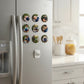 A collection of colorful personalized round photo button pins displayed neatly on the door of a white kitchen refrigerator next to a glass jar.