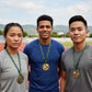 Three focused track and field athletes standing together proudly outdoors at a sports stadium complex while wearing their custom engraved gold tournament championship medallions.