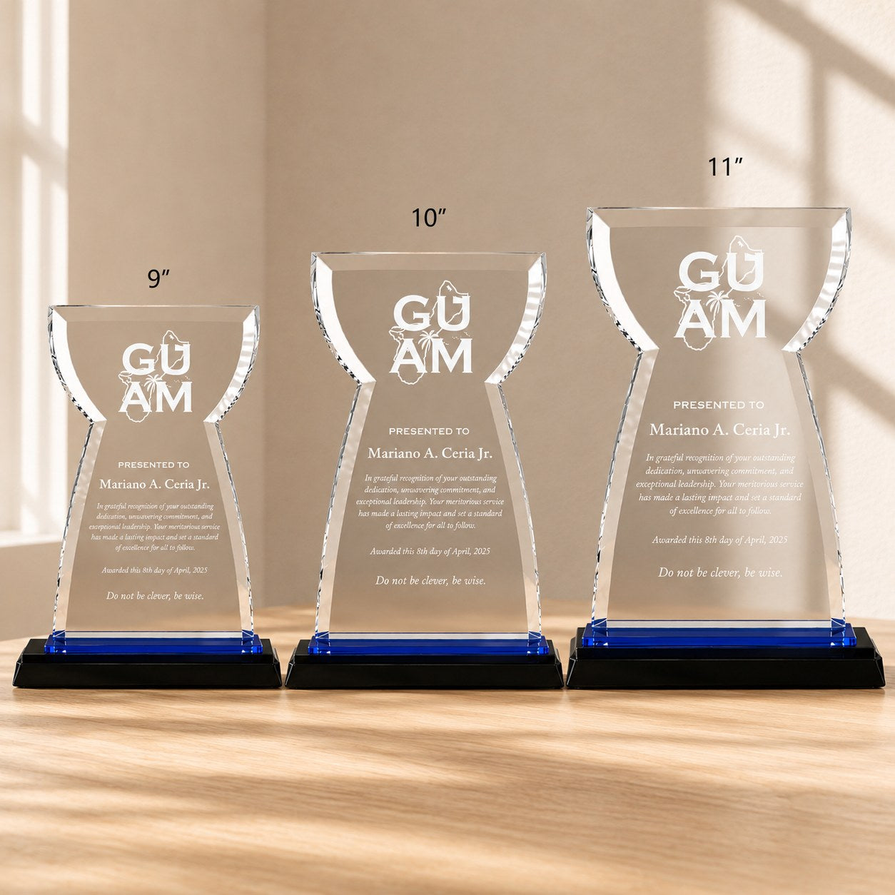 Three Guam crystal award plaques with blue and black bases in 9-inch, 10-inch, and 11-inch sizes displayed on a light oak tabletop in a premium daylight setting, ideal for corporate recognition and employee achievement awards.