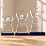 Three Guam crystal award plaques with blue and black bases in 9-inch, 10-inch, and 11-inch sizes displayed on a light oak tabletop in a premium daylight setting, ideal for corporate recognition and employee achievement awards.