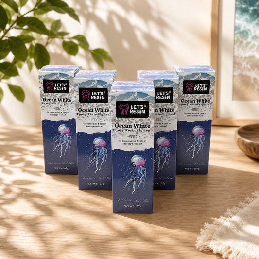 A collection of five boxes of Let's Resin Ocean White Pigment liquid ink display containers featuring jellyfish illustrations, arranged neatly on a wooden table next to a decorative plant.