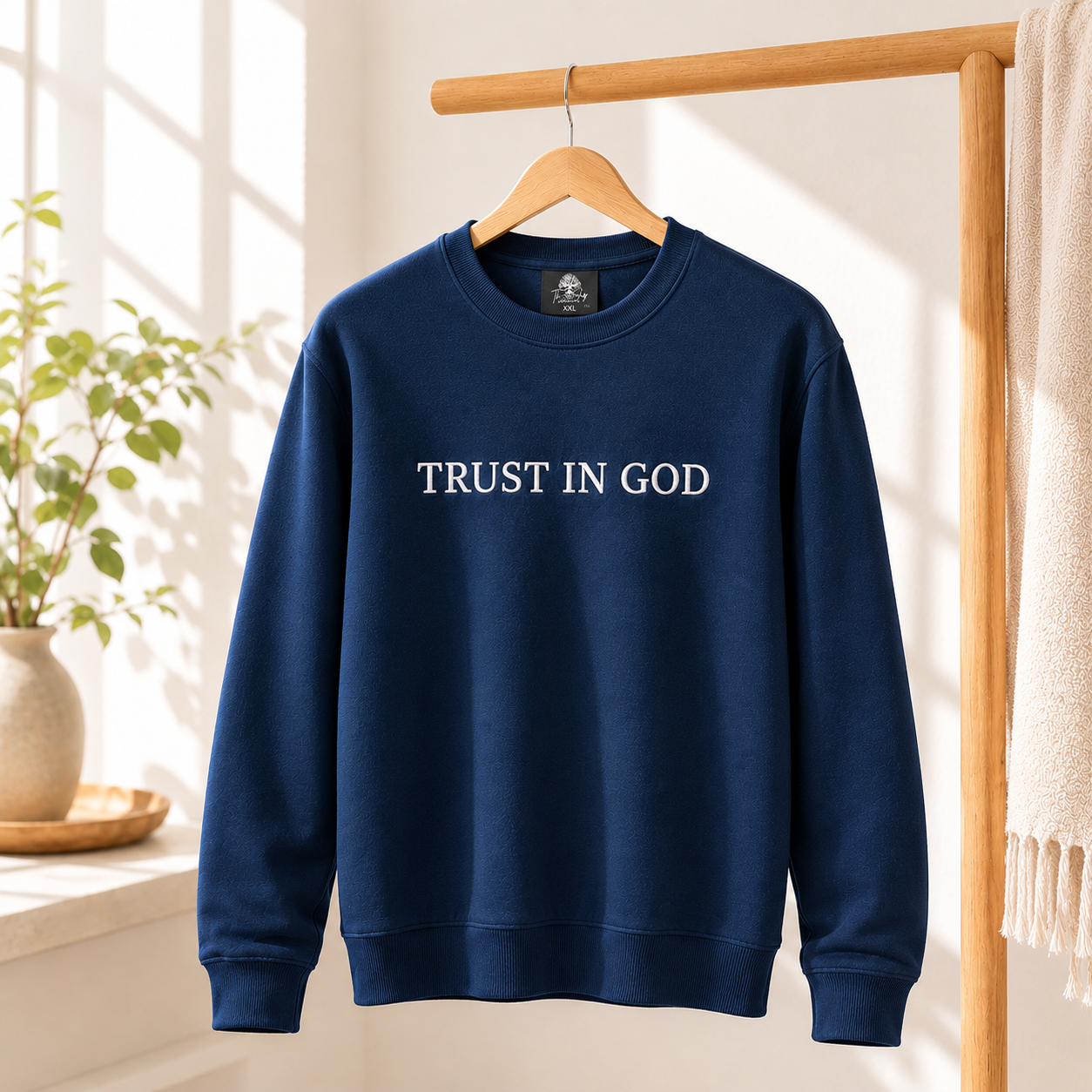 Close-up shot of a premium navy blue crewneck sweater featuring high-quality white embroidered text that reads 'TRUST IN GOD' across the chest chest area.