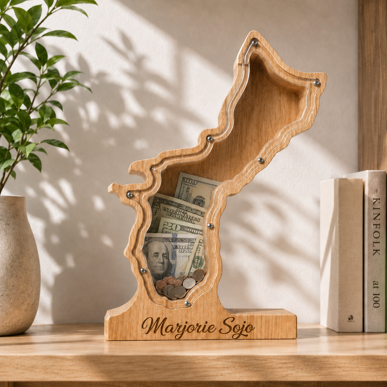 The personalized Guam Island wooden shadow box savings bank displayed on a wooden shelf, filled with folded dollar bills visible behind the clear acrylic front panel.