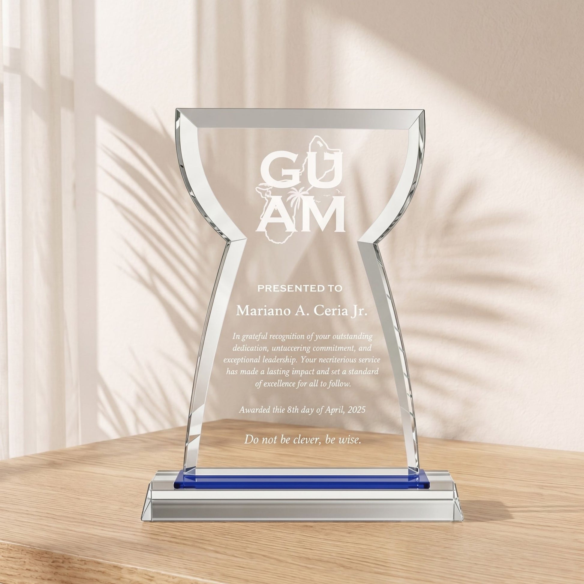 A premium 9x7 inch custom laser-engraved crystal glass award plaque shaped like an iconic Guam latte stone with an elegant blue accent base, standing on a wooden office desk under natural window light.