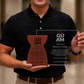A man in a black polo shirt holding the custom personalized crystal glass and wooden latte stone recognition award, showcasing the clean white engraved lettering up close.