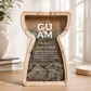 The personalized latte stone wooden savings piggy bank displayed on a table, filled with dollar bills visible behind the clear acrylic front panel custom printed with 'GUAM' branding.